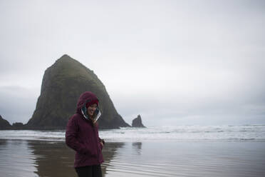 Happy woman in warm clothing standing on shore against sky - CAVF72444