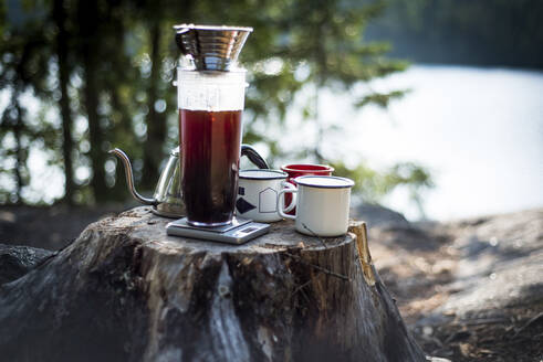 Nahaufnahme von Kaffeetassen und Wasserkocher auf einem Baumstumpf auf dem Campingplatz - CAVF72458