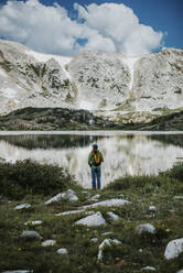 Rear view of hiker with backpack standing at lakeshore against Medicine Bow Mountains - CAVF72475