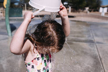 Mädchen leert Eimer mit Wasser auf den Kopf im Park - CAVF72480