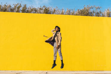 Young man dancing in front of yellow wall, jumping mid air - AFVF04530