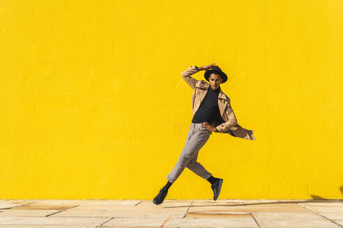 Young man dancing in front of yellow wall, jumping mid air - AFVF04542