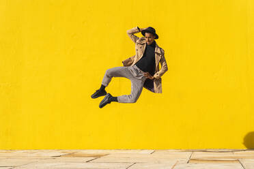 Young man dancing in front of yellow wall, jumping mid air - AFVF04544