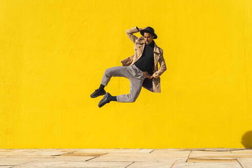 Junger Mann tanzt vor einer gelben Wand und springt in der Luft - AFVF04544
