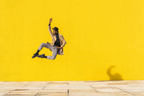 Junger Mann tanzt vor einer gelben Wand und springt in der Luft - AFVF04545