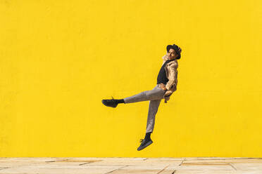 Young man dancing in front of yellow wall, jumping mid air - AFVF04547