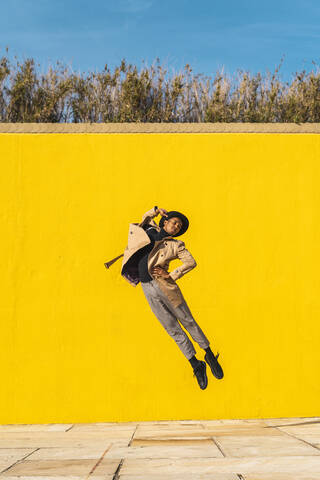 Junger Mann tanzt vor einer gelben Wand und springt in der Luft, lizenzfreies Stockfoto