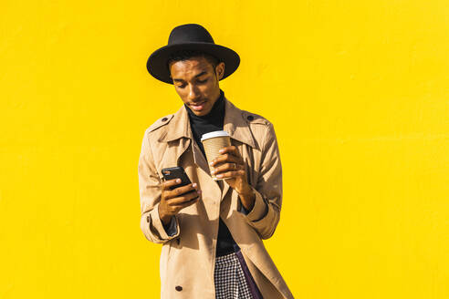 Junger Mann mit Kaffeetasse, der sein Smartphone benutzt - AFVF04568