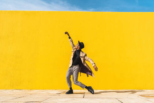 Junger Mann tanzt vor einer gelben Wand und macht Selfies - AFVF04574