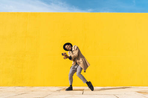 Young man dancing in front of yellow wall, taking selfies - AFVF04575