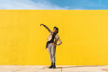 Junger Mann tanzt vor einer gelben Wand und macht Selfies - AFVF04576