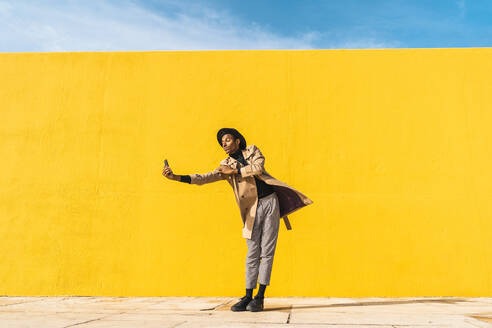 Young man dancing in front of yellow wall, taking selfies - AFVF04578