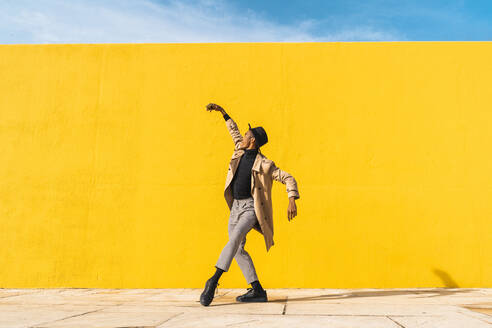 Young man dancing in front of yellow wall, taking selfies - AFVF04579