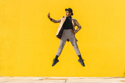 Junger Mann tanzt vor einer gelben Wand und macht Selfies - AFVF04581