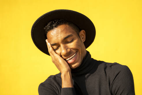 Porträt eines jungen Mannes, schwarz gekleidet, vor einer gelben Wand, die Hand im Gesicht - AFVF04590
