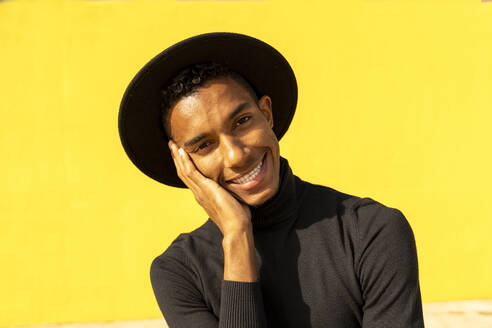 Portrait of young man, wearing black in front of yellow wall, hand on face - AFVF04591