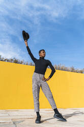 Young man with black hat, dancing in front of yellow wall - AFVF04594