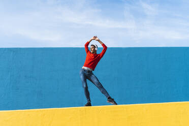 Junger Mann mit Kopfhörern, der Musik hört und auf einer gelben Wand tanzt - AFVF04603