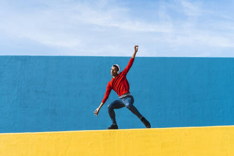 Young man with headphones, listening music, dancing on yellow wall stock photo