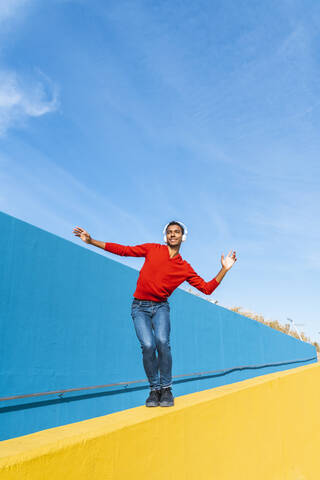 Junger Mann mit Kopfhörern, der Musik hört und auf einer gelben Wand tanzt, lizenzfreies Stockfoto