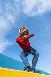 Young man with headphones, listening music, dancing on yellow wall - AFVF04610