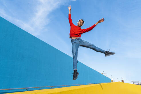 Young man with headphones, listening music, dancing on yellow wall - AFVF04613