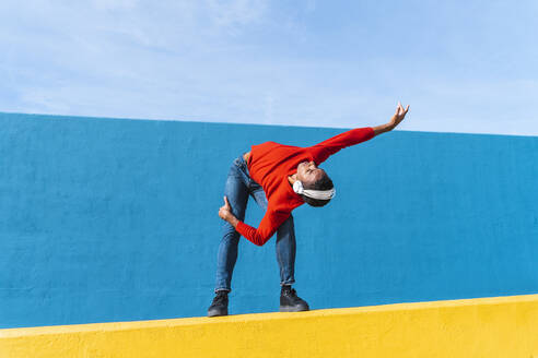Young man with headphones, listening music, dancing on yellow wall - AFVF04616