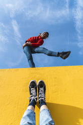 Young man with headphones, dancing for person, leaning on yellow wall - AFVF04618