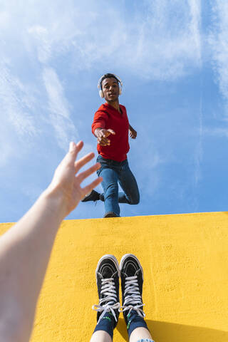 Young man with headphones, dancing for person, leaning on yellow wall stock photo