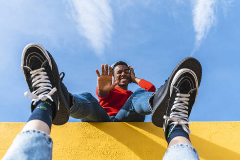 Young man with headphones, dancing for person, leaning on yellow wall - AFVF04621