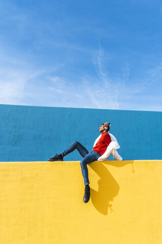 Junge Tänzerin sitzt auf gelber Wand und hört Musik, lizenzfreies Stockfoto