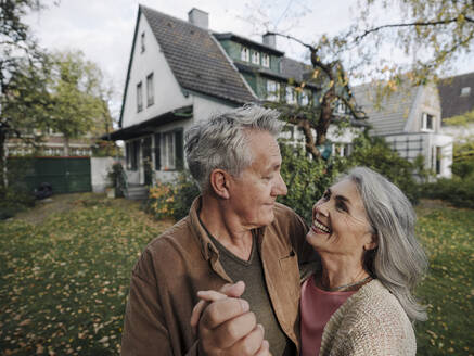 Happy senior couple in garden of their home in autumn - GUSF02975