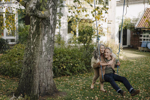 Glückliche Frau umarmt älteren Mann auf einer Schaukel im Garten, lizenzfreies Stockfoto