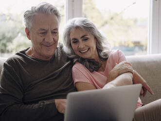 Happy senior couple with laptop relaxing on couch at home - GUSF02989