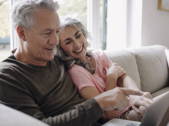 Happy senior couple with laptop relaxing on couch at home - GUSF02990