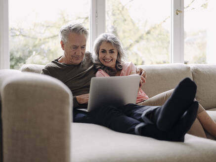 Happy senior couple with laptop relaxing on couch at home - GUSF02991