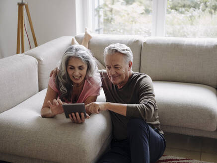 Glückliches älteres Paar, das sich zu Hause auf der Couch entspannt und ein Tablet benutzt - GUSF02999