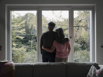 Rear view of senior couple looking out of window at home - GUSF03012