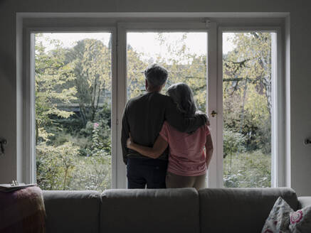 Rear view of senior couple looking out of window at home - GUSF03012