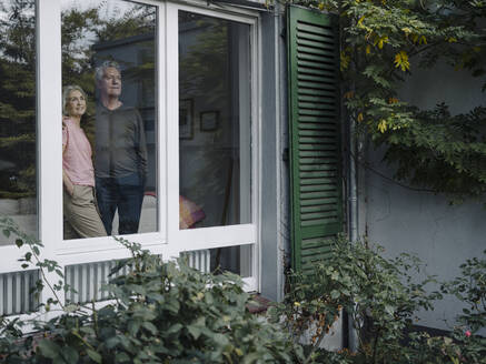 Senior couple behind windowpane of their home looking out - GUSF03013