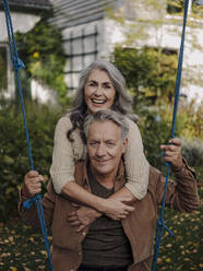 Happy woman embracing senior man on a swing in garden - GUSF03020