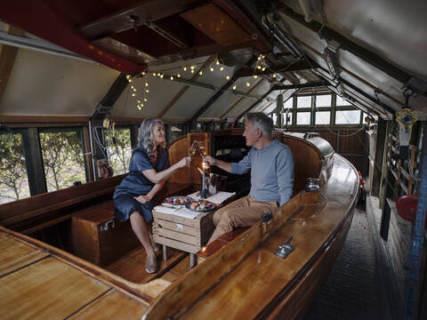 Senior couple having a candlelight dinner on a boat in boathouse clinking champagne glasses stock photo