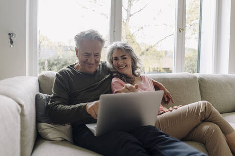 Glückliches älteres Paar mit Laptop, das sich zu Hause auf der Couch entspannt, lizenzfreies Stockfoto