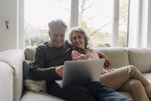 Happy senior couple with laptop relaxing on couch at home - GUSF03037