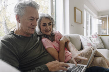 Happy senior couple with laptop relaxing on couch at home - GUSF03038