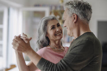 Glückliches älteres Paar tanzt im Wohnzimmer zu Hause - GUSF03042