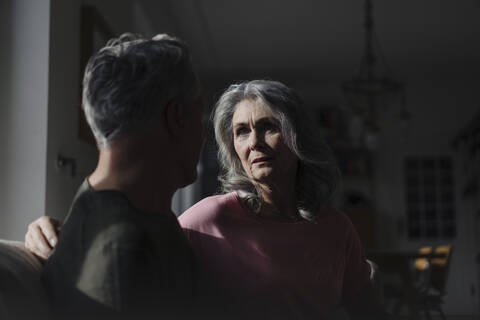 Serious senior couple sitting on couch at home in shadow stock photo