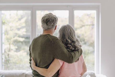Rückansicht eines älteren Paares, das aus dem Fenster seines Hauses schaut, lizenzfreies Stockfoto