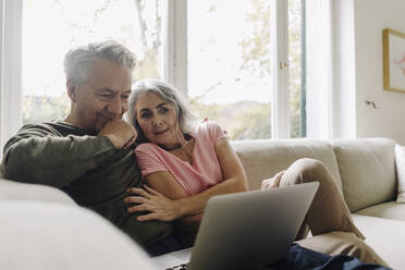 Senior couple looking at laptop on couch at home - GUSF03060