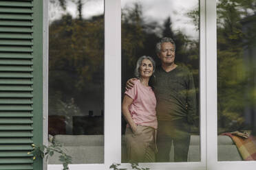 Senior couple behind windowpane of their home looking out - GUSF03062